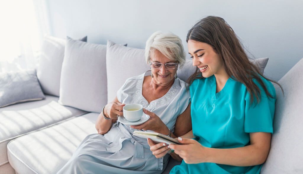 Home healthcare worker has tea with elderly woman.