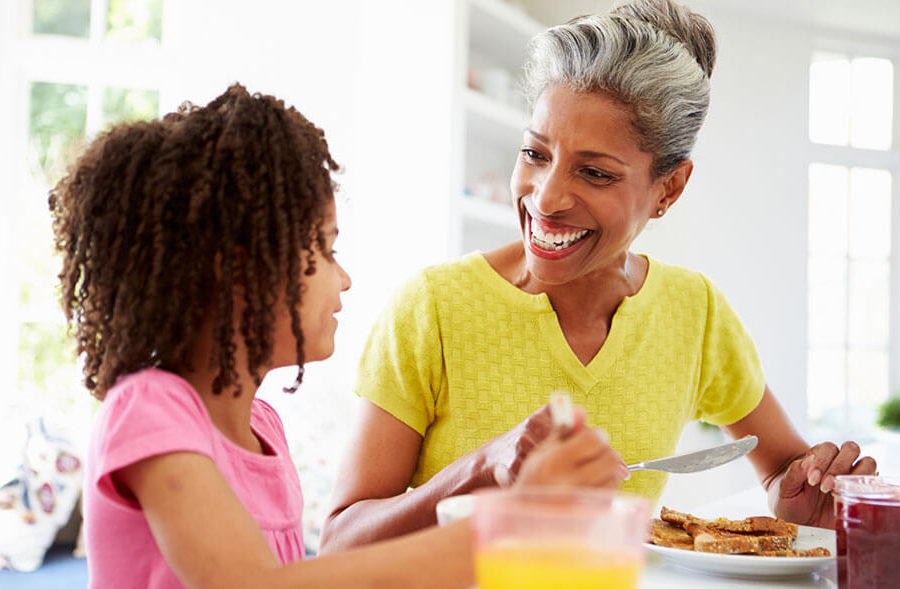Grandmother eats breakfast with granddaughter at home.